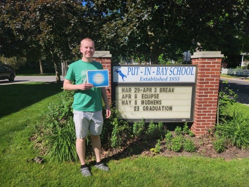 Emil Michael standing outside school with award in hand